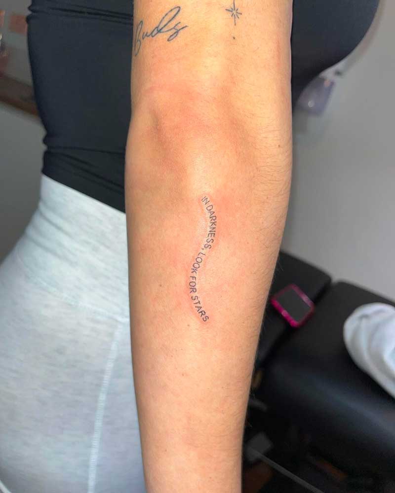 Tatouage de citation inspirante en écriture délicate sur l'avant-bras intérieur, indiquant « pas d'obscurité, pas d'étoiles » avec un petit symbole d'étoile.